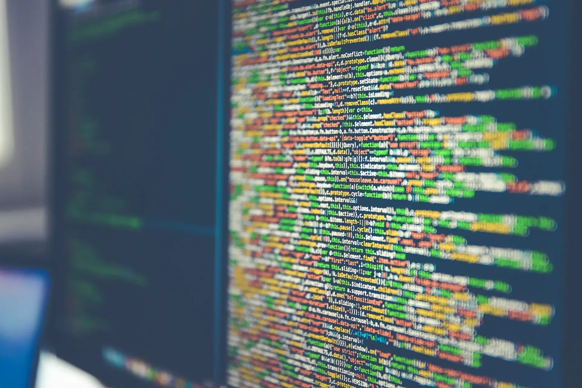 Zbliżenie na monitor z kolorowo podświetlonym kodem, ujęcie pod kątem z rozmytym drugim ekranem w tle